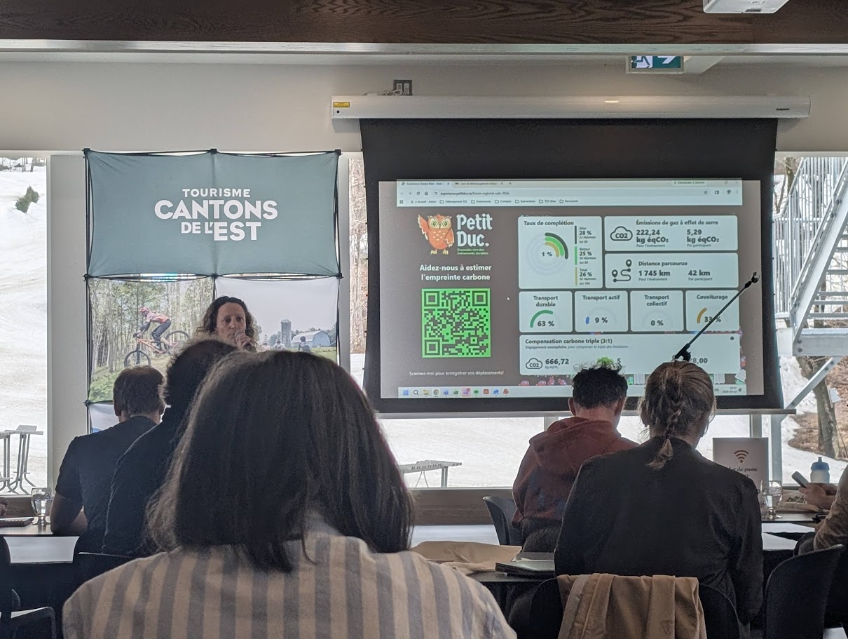 Photo of a presentation of the Petit Duc dashboard to a group of attendees, with the Tourisme Cantons-de-l’Est banner in the background.